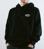 Mann trägt schwarzen O'Donnell Moonshine Hoodie – Frontalansicht mit weißem Logo-Aufdruck auf der Brust, helle Hintergrundaufnahme